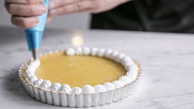 En baker som legger den glatte marengsblandingen på sitronmarengspaien