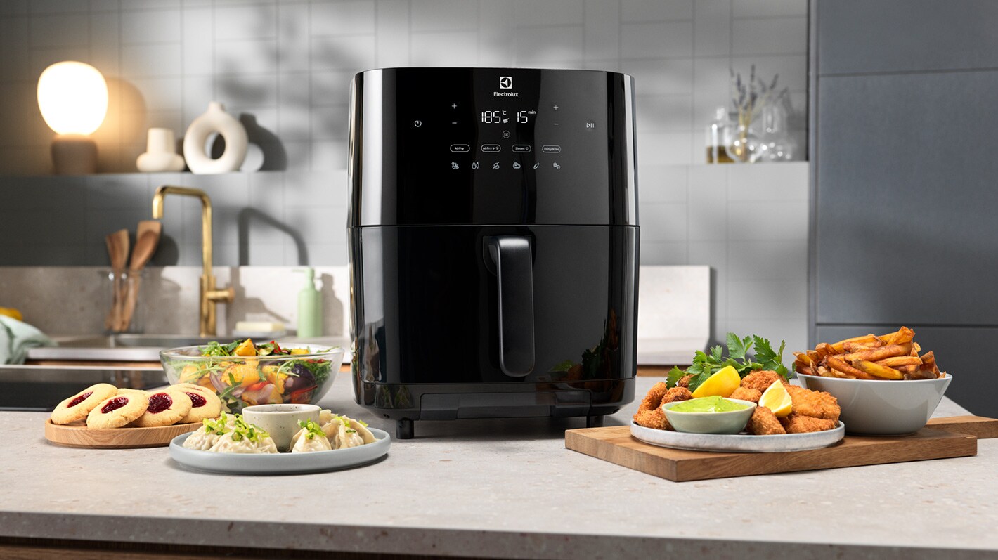 En airfryer står på en kjøkkenbenk, omringet av flere ulike matretter.