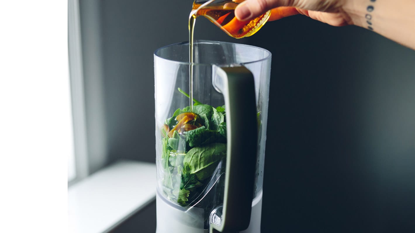 En person heller honning i en blender med grønnsaker og urter i.