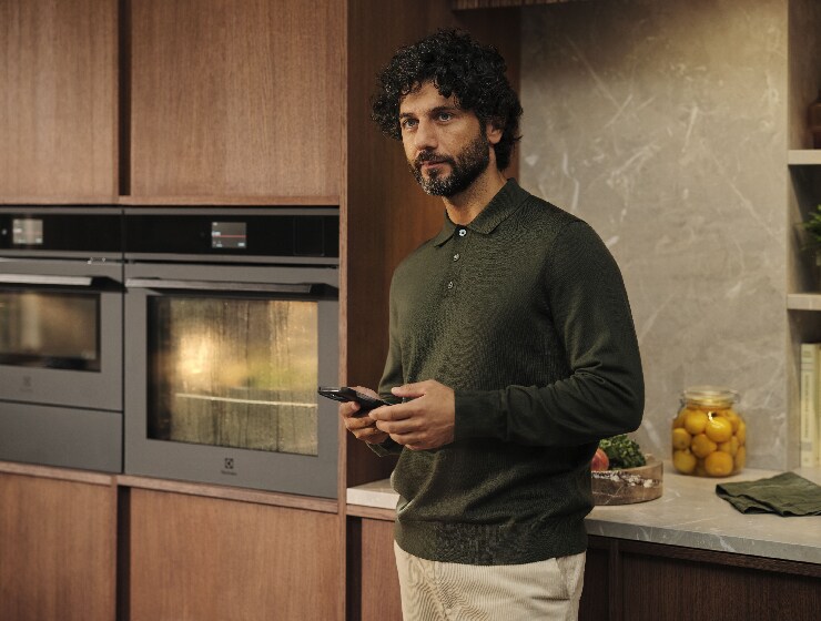 Mann som står i kjøkkenet og holder en telefon