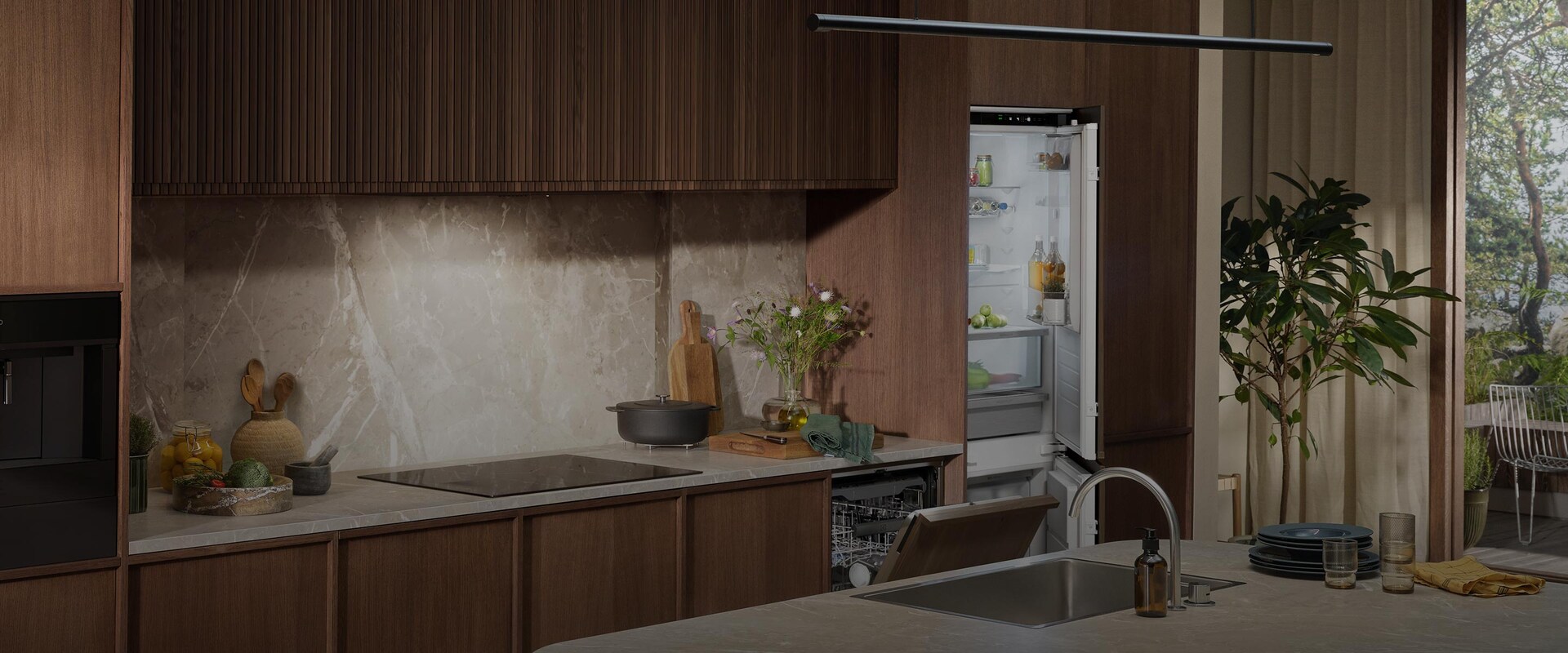 Integrert kombiskap og oppvaskmaskin i et stilrent kjøkken med mørke trepaneler og benkeplate i marmor.