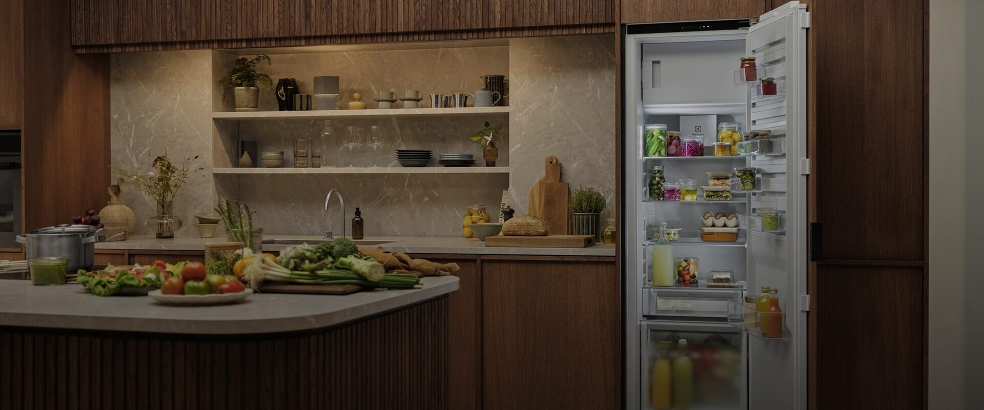 Oversikt over et åpent, integrert Electrolux-kjøleskap i et moderne kjøkken, fylt med ferske råvarer, flasker og organiserte matbokser.