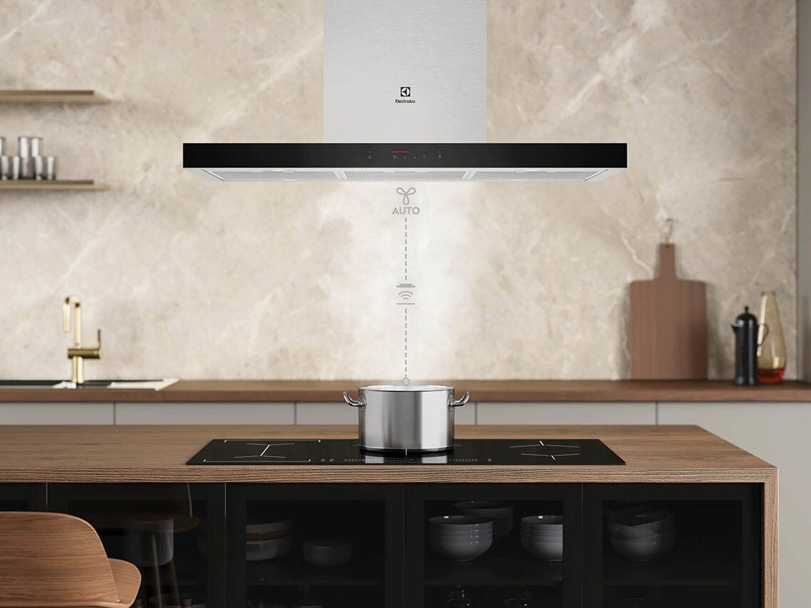 Fritthengende kjøkkenventilator over kjøkkenøy med kokende kasserolle; grafikk med teksten «AUTO» illustrerar Hob2Hood-funksjonen.