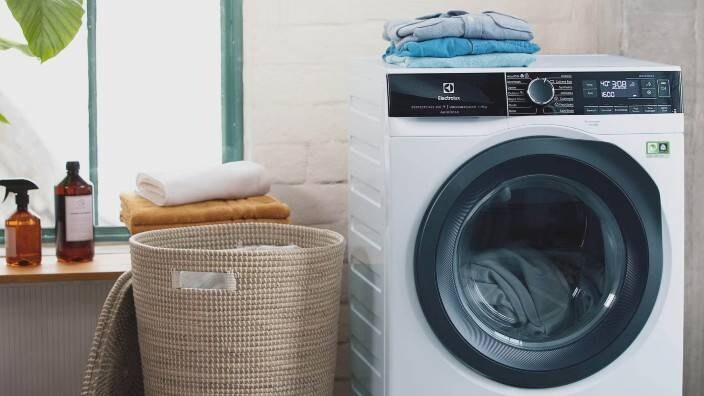 En vaskemaskin fra Electrolux holder på med en klesvask. Ved siden av ligger brettede klær.