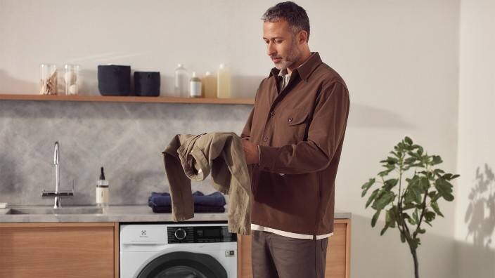 En mann som holder en brun skjorte i hendene. I bakgrunnen ser man en vaskemaskin fra Electrolux.