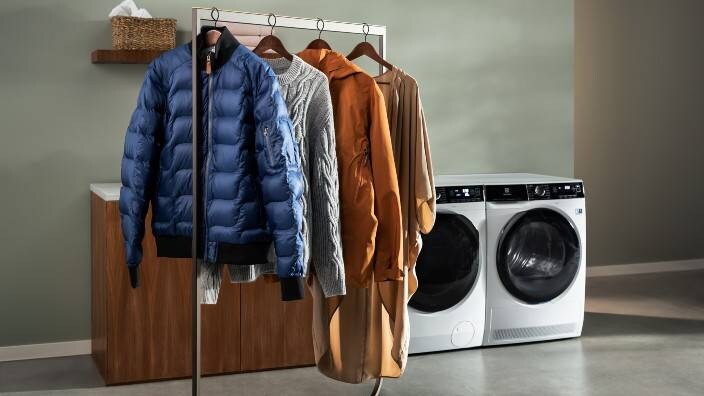 Fire klesplagg henger på et stativ. I bakgrunnen står en vaskemaskin og tørketrommel.