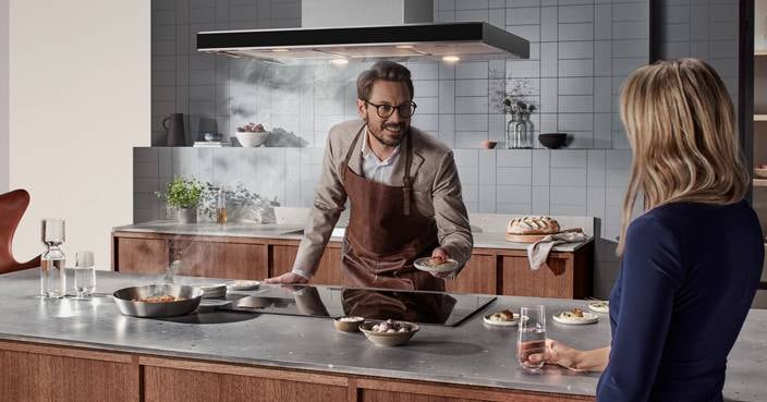 En mann og en kvinne står og prater på et kjøkken mens de lager mat.