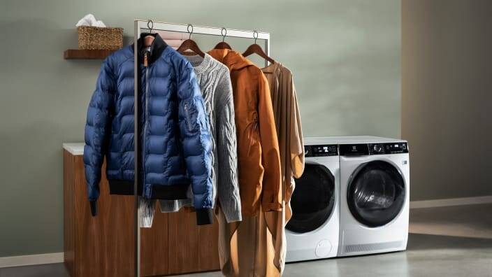 Klesplagg henger på et klesstativ ved siden av en vaskemaskin og tørketrommel.
