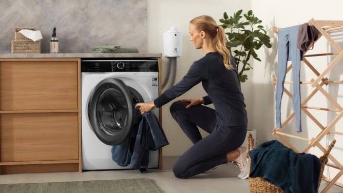 Kvinne som legger klesvask i en vaskemaskin